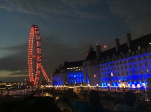The London Eye, lit in red, sits next to another building lit in blue along the Thames
