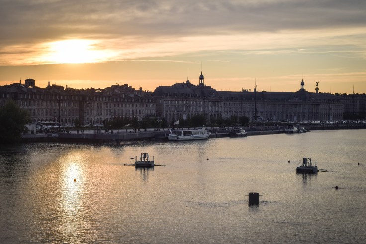 Sun sets over the even and unbroken skyline of Bordeaux from the bridge over the river
