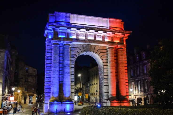 A triumphal arch in Bordeaux lit in blue, white, and red