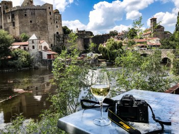 My glass of wine and camera in front of the river, bridge, and castle of Clisson