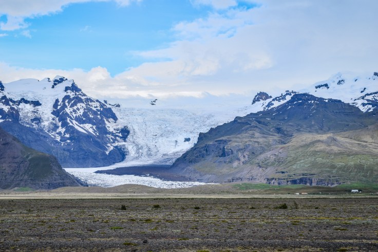 A wide blue glacier creeping slowly down a mountainside in Iceland