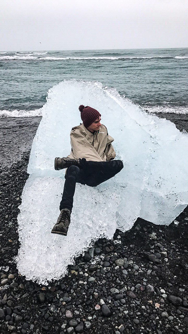 Me dressed in boots and a rain jacket sitting on a large chunk of ice from the glaciers in Iceland